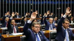 Cena de plenário do Congresso com deputados votando, destacando mãos levantadas e expressão séria, falando sobre regulamentação reforma tributária PLP
